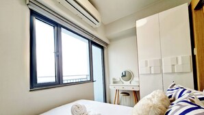 Habitació d'hotel amb un llit gran, una finestra amb persianes, escriptori amb mirall i un armari.