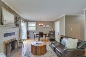 A living room with a fireplace, a round coffee table, a leather sofa, and a dining area with chairs and a table. - Charlottesville Getaway in Bailey's Retreat! (Charlottesville)