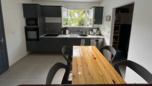 A compact kitchen with a wooden dining table, dark cabinets, and a window with a view of greenery.