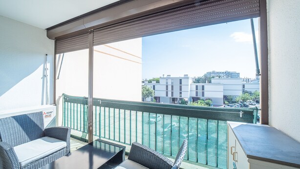 Un balcon doté de meubles en osier, offrant une vue sur les immeubles et agrémenté d’une rambarde verte.