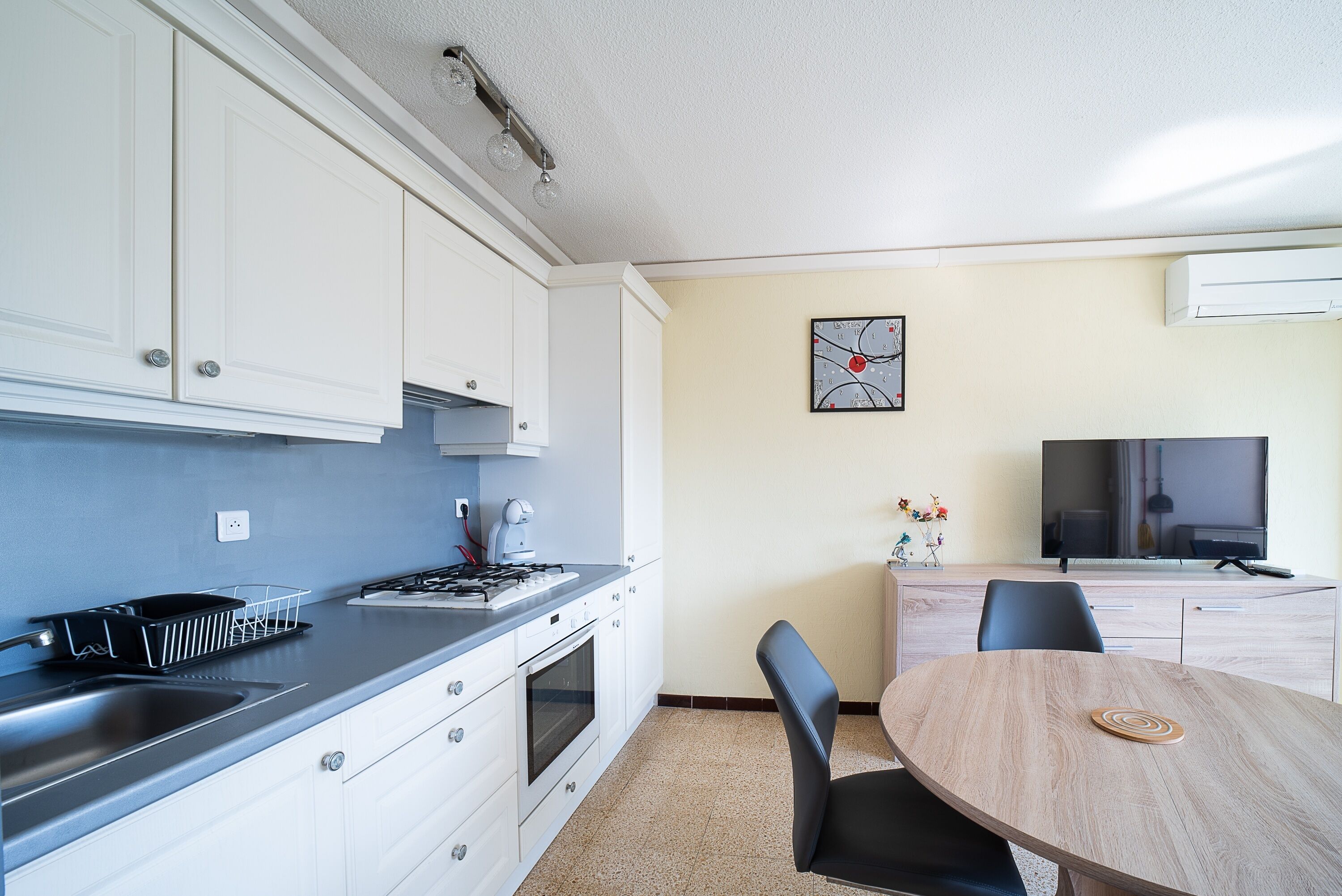 A modern kitchen with white cabinets, a stove, and a sink. There is a dining area with a wooden table and chairs.