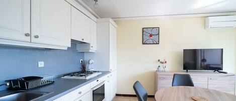 A modern kitchen with white cabinets, a stove, and a sink. There is a dining area with a wooden table and chairs.