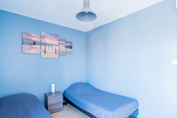 Un dormitorio con dos camas, una mesita de noche y una lámpara fijada a la pared.