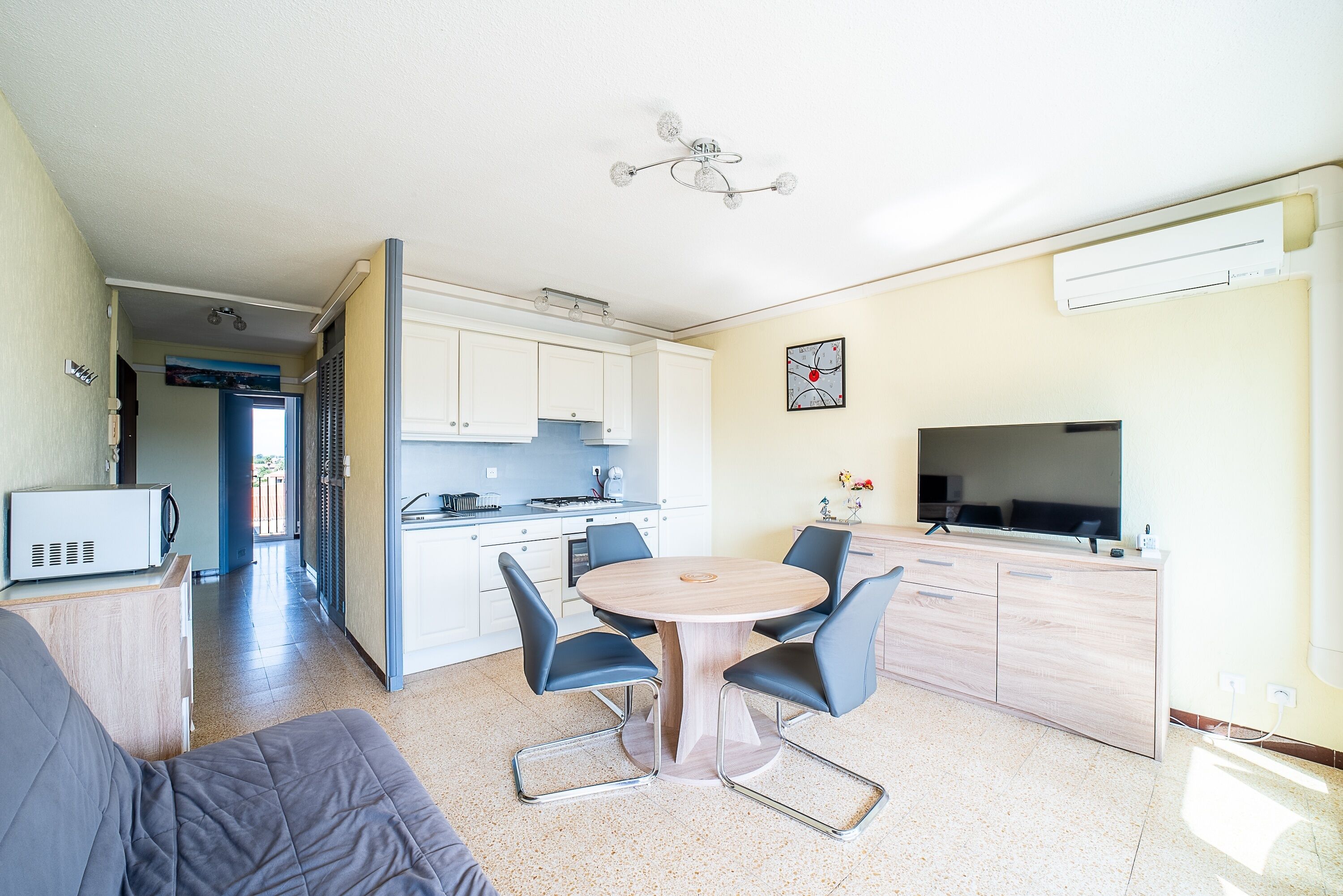 Un espacio habitable compacto con kitchenette, un comedor con mesa redonda y sillas, un televisor y un microondas.