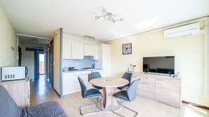 Un espace de vie compact comprenant un coin cuisine, un coin repas avec une table ronde et des chaises, un téléviseur et un four à micro-ondes.