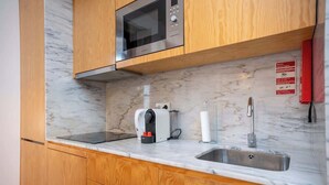 Een kleine keuken met houten kastjes, een roestvrijstalen magnetron, een koffiezetapparaat en een spoelbak.