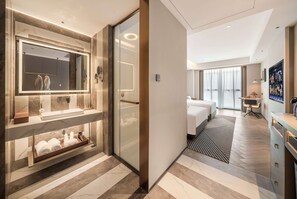 A modern hotel bathroom with a large mirror, a vanity with a sink, and a towel rack. The room has a large bed and a desk with a chair. - Howard Johnson Life Hotel by Wyndham Chongqing Liangjiang (Chongqing)