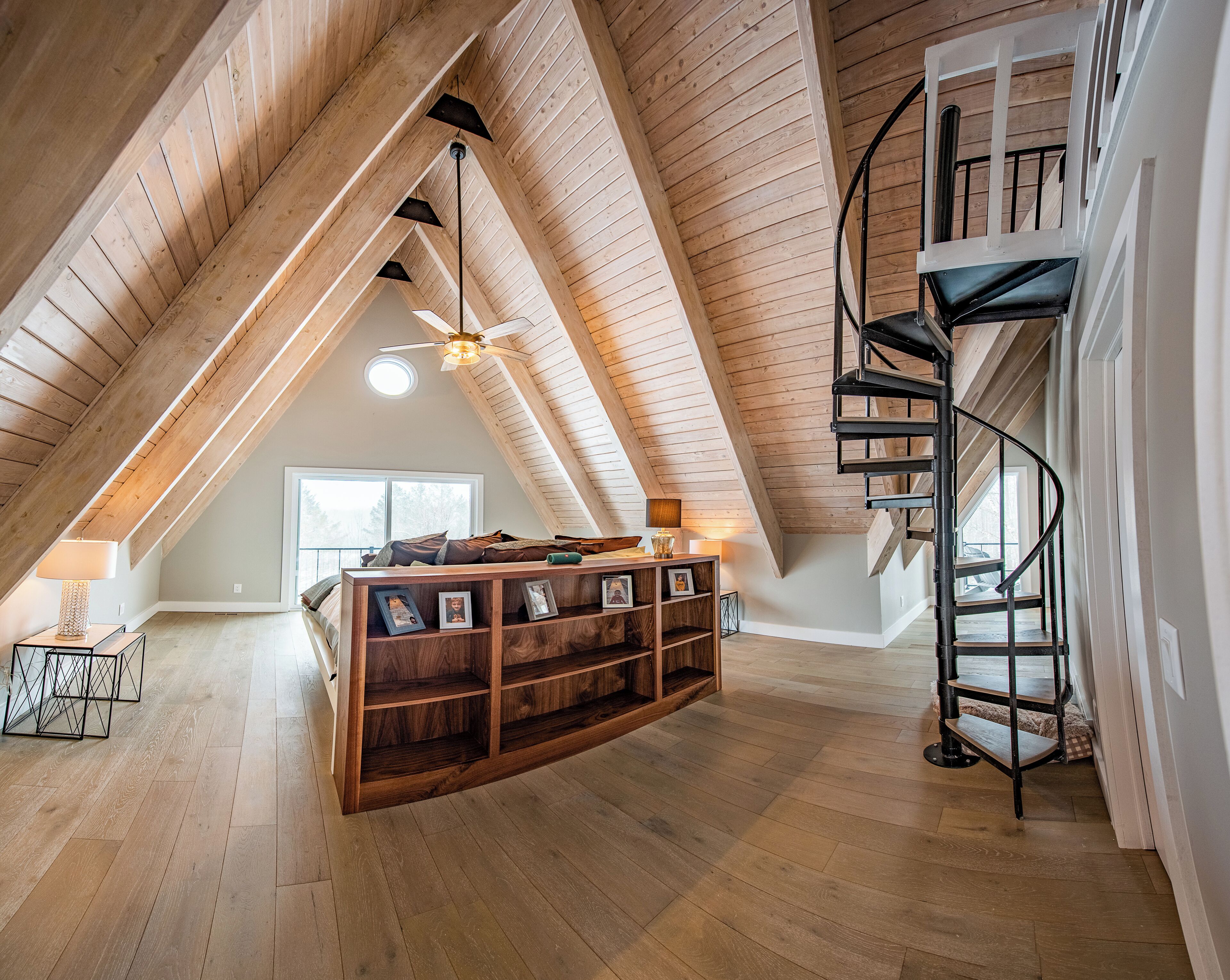 Et soveværelse med skrå væg og loft i træ, en indbygget seng, en spiraltrappe og et skydelys.
