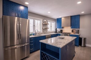 A modern kitchen with stainless steel appliances, blue cabinetry, and a granite countertop island. - Lakefront 3BR Luxury Home at High Bluffs (Leland)
