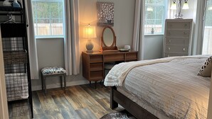 A bedroom with a wooden floor, a bed with a white bedspread, a dresser, a mirror, and a lamp.