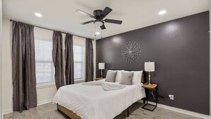 Una camera da letto con un letto, una ventola a soffitto, una sveglia a muro e una finestra con tende.