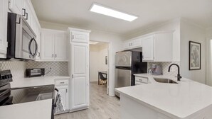 Una cucina moderna con mobili bianchi, elettrodomestici in acciaio inossidabile e una grande isola con lavello.