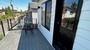 En overdækket terrasse med et bord og stole, en sort dør og udsigt til nabolaget.