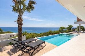 A modern pool area with a clear view of the ocean, a palm tree, and lounge chairs. - Luxury 12-Guest Villa: Pool, Oceanview & Beach (Bandabou)