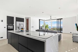 Une cuisine moderne dotée d’un grand îlot central, d’appareils électroménagers intégrés et offrant une vue sur l’océan.
