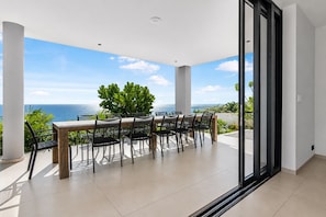 A spacious balcony with a dining table and chairs, overlooking a scenic ocean view. - Luxury 12-Guest Villa: Pool, Oceanview & Beach (Bandabou)