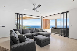 A modern living room with a sectional sofa, a ceiling fan, and a view of the ocean.