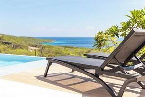 Eine Liege am Pool mit Blick auf das Meer und einen klaren Himmel.