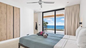 Ein Schlafzimmer mit Bett, Deckenventilator, Meerblick und einer Schiebetür.