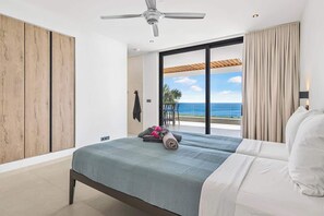 Ein Schlafzimmer mit Bett, Deckenventilator, Meerblick und einer Schiebetür.