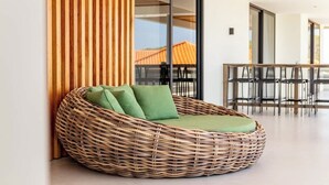 Ein rattengewebtes Sofa mit grünen Kissen in einem modernen Innenraum.