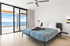 Une chambre moderne avec un grand lit, un ventilateur de plafond et une vue sur l’océan.
