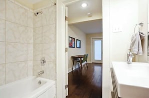 A bathroom with a bathtub, a shower, and a sink. There is a dining area visible in the background. - Cute 1bed steps from French Q, Bourbon St & Jazz venues (New Orleans)