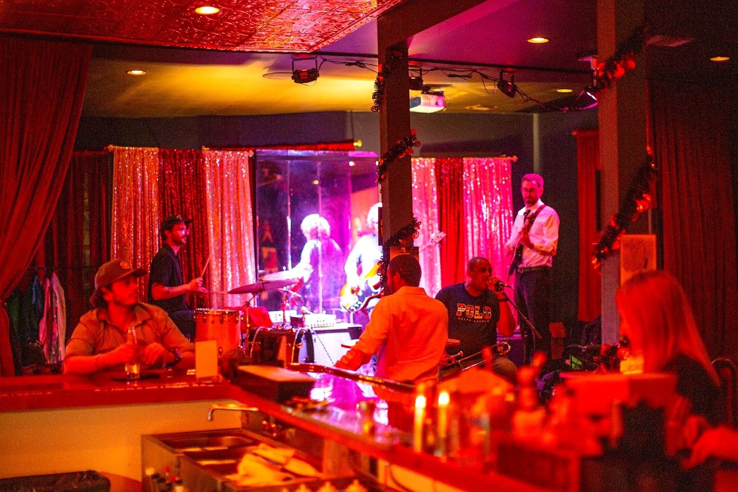 A bar area with a stage for live music, a bartender, and patrons.