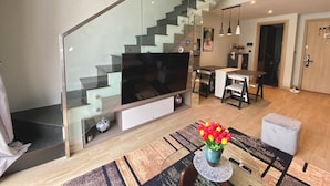 A modern living room with a glass staircase, a flat-screen TV, a dining area, and a small table with a vase of flowers. - Sandy Homestay Citadines Marina Ha Long is a great choice for accommodation (Ha Long)