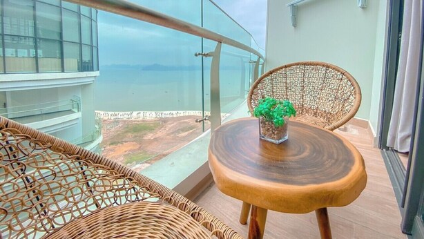 A balcony with wicker furniture, a small wooden table with a plant, and a view of the sea. - Sandy Homestay Citadines Marina Ha Long is a great choice for accommodation (Ha Long)