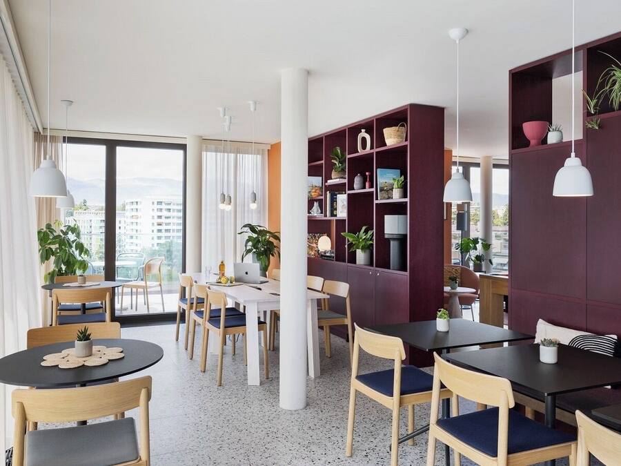 Un comedor moderno con mesas y sillas redondas, una estantería y vistas a la ciudad.