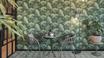 A room with a patterned wall, two wicker chairs, a small round table, a potted plant, and a floor lamp.
