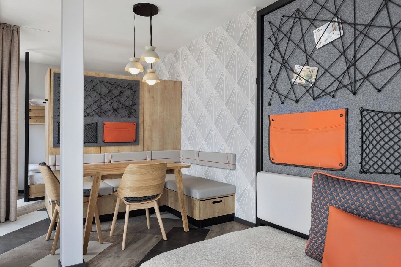 Una habitación moderna con una mesa de comedor de madera, dos sillas, un banco y un sofá. Hay un estante fijado a la pared con un diseño geométrico y un bolso pequeño naranja.