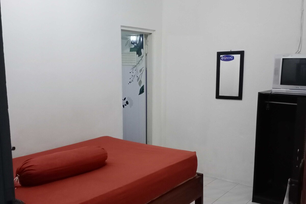 Une chambre avec un lit simple, un petit bureau avec une télévision et une porte sur laquelle est apposée une pancarte.