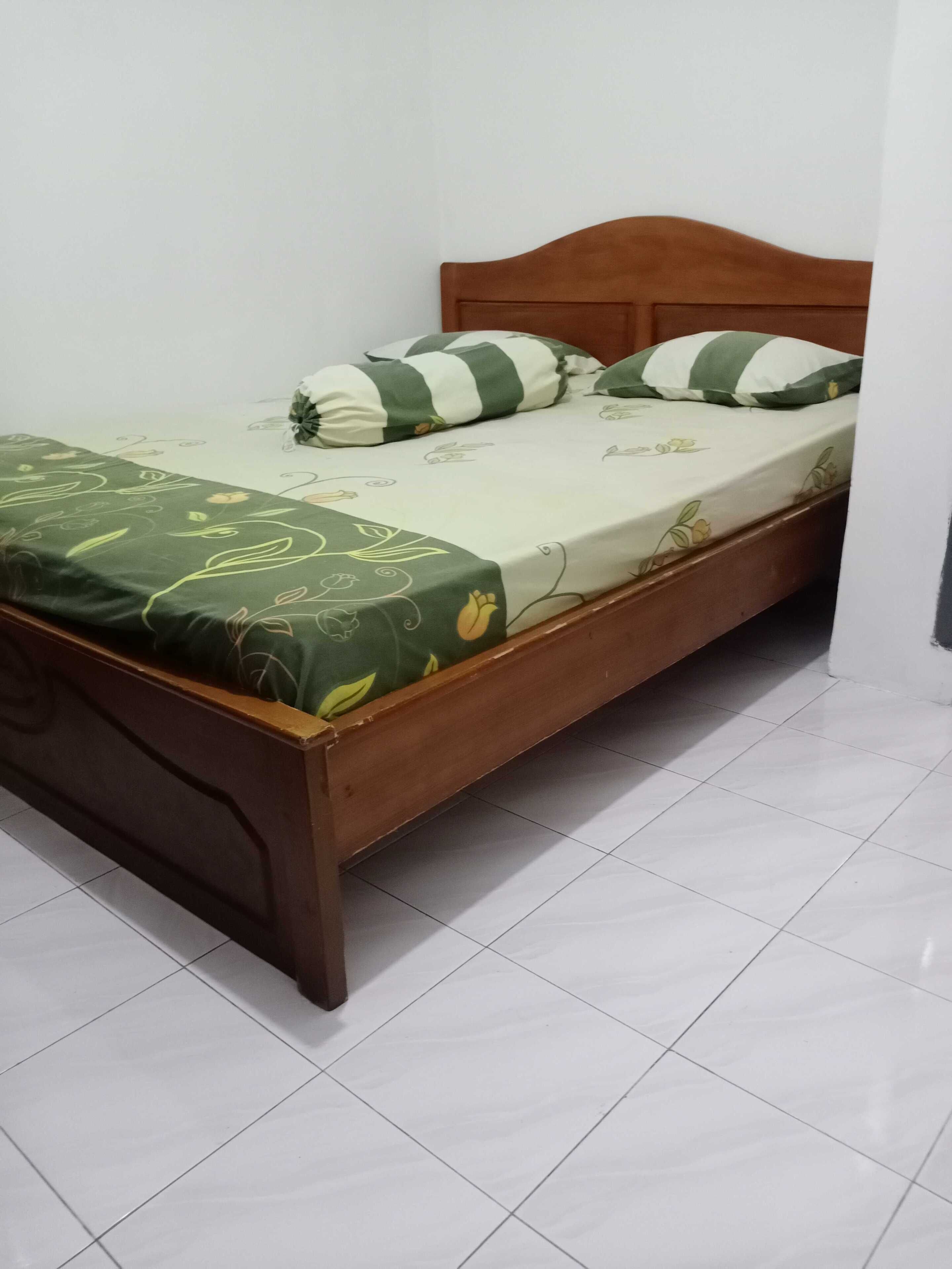 Una cama individual con estructura de madera, colcha floral verde y dos almohadas a rayas.
