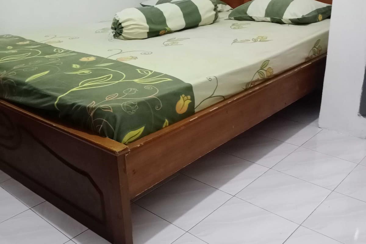 Un lit simple avec un cadre en bois, une couvre-lit à motifs floraux verts et deux coussins à rayures.