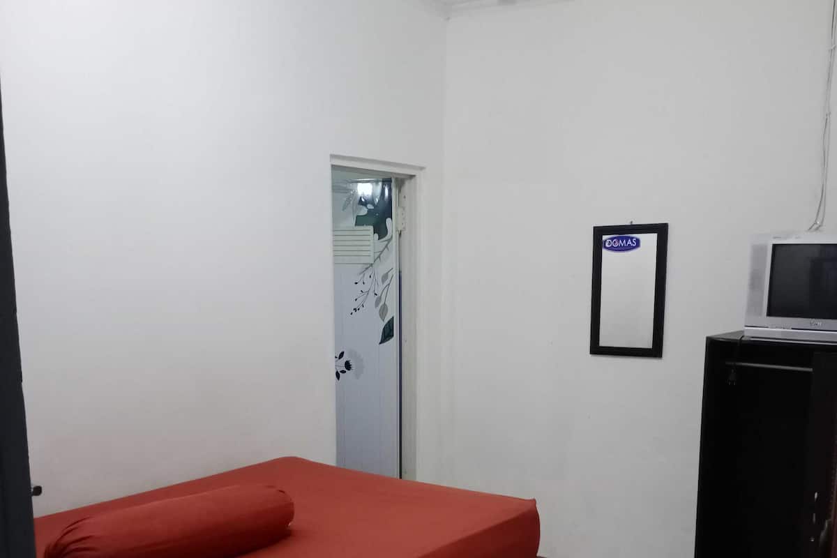 Une chambre avec un lit simple, un petit bureau avec une télévision et une porte sur laquelle est apposée une pancarte.
