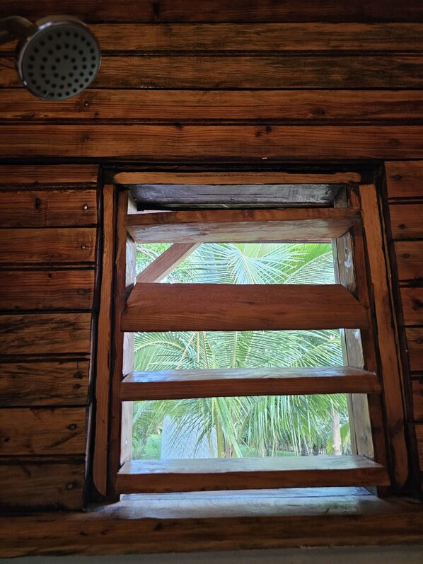 A wooden window with a metal grill, framed by wooden beams, overlooking a lush green landscape.