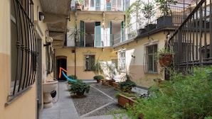 Un patio estrecho con macetas, suelo de baldosas y una puerta que da a un espacio interior.