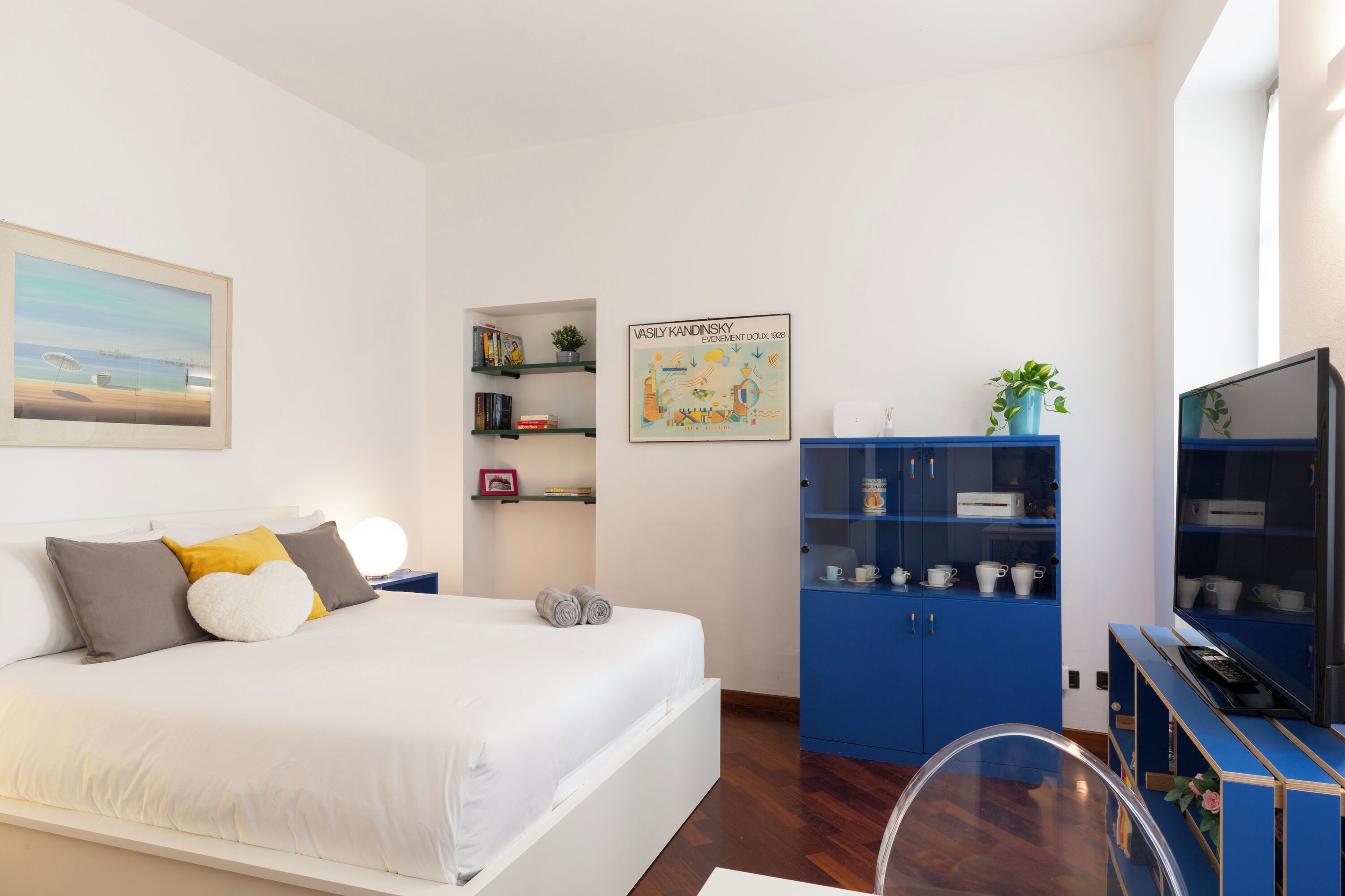 A bedroom with a bed, a blue cabinet, a TV, and a painting on the wall.
