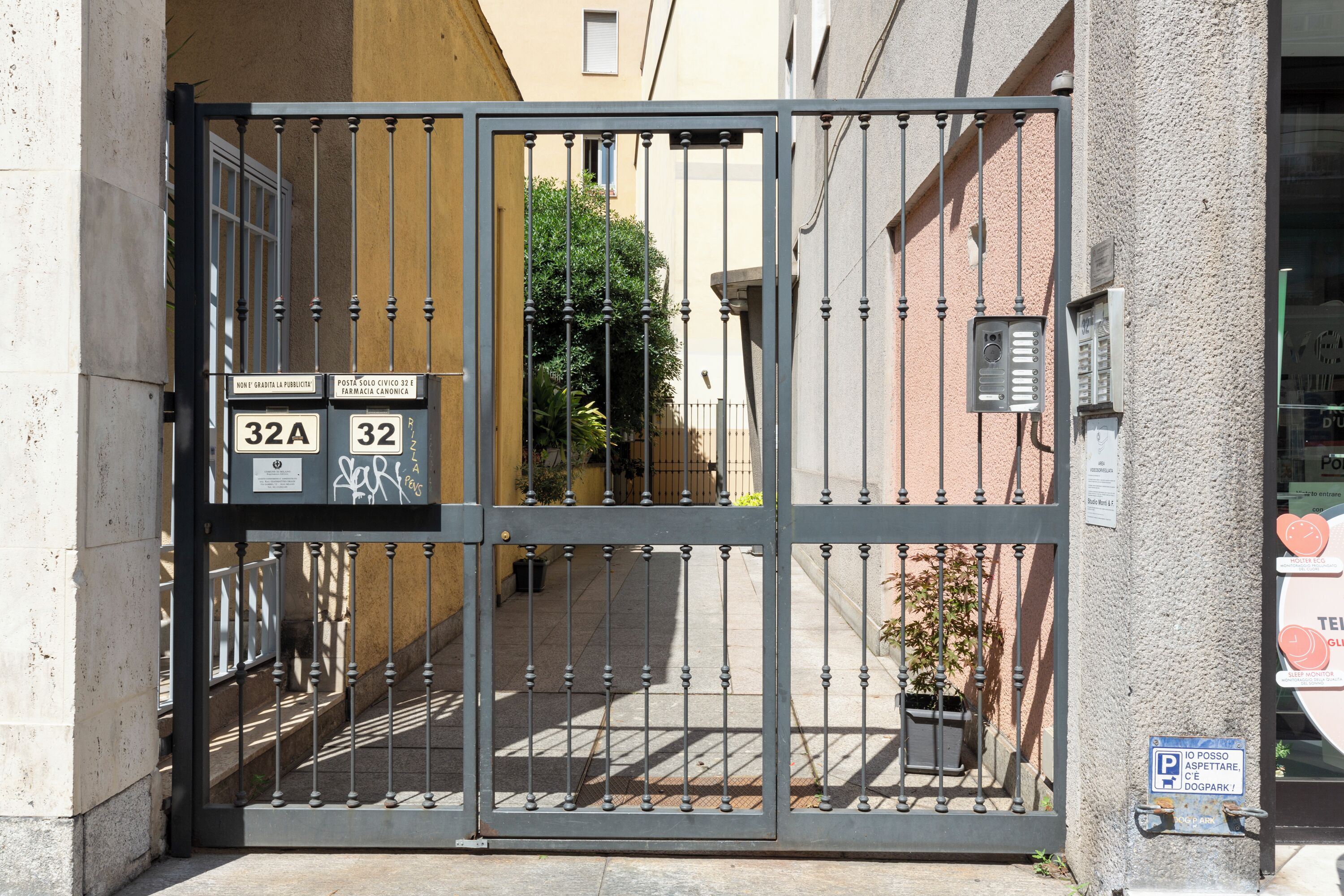 Una entrada protegida por un portón metálico, una planta en maceta y un letrero que indica un parque canino.