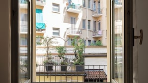 Vista desde una ventana de un edificio de varios pisos, con balcones, plantas en macetas y tejado de tejas.