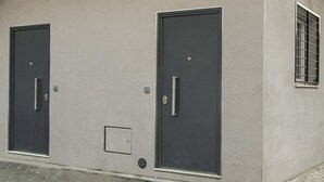 Två mörkfärgade dörrar med handtag, ett litet fönster med ett metallgaller och en ventil på väggen.
