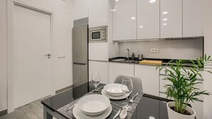 Ett modernt kök med vita skåp, en mikrovågsugn och en matplats med ett glasbord där det är dukat för två personer.