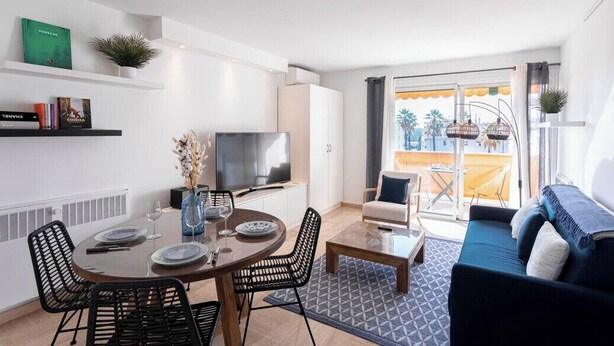 A modern living room with a dining area, a sofa, a TV, and a balcony with a view. - Cocoon with garden near the sea (Cannes)