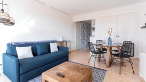A living room with a blue sofa, a wooden coffee table, and a dining area with a table and chairs. - Cocoon with garden near the sea (Cannes)