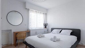 A modern bedroom with a large bed, a round mirror, a wooden chair, and a window with curtains. - Cocoon with garden near the sea (Cannes)