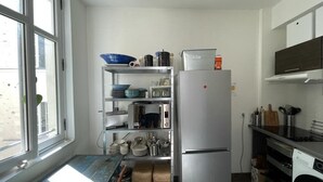 Eine kleine Küche mit einem Kühlschrank, Regalen mit Geschirr und einem Fenster.