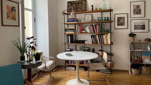 Ein Zimmer mit einem runden weißen Tisch, zwei Stühlen, einem Bücherregal und einem Fenster.