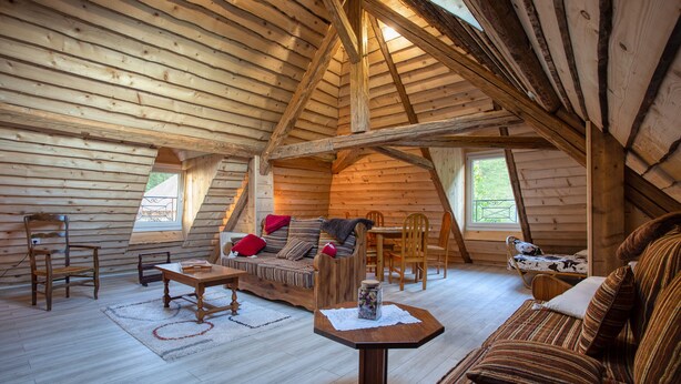 A cozy log cabin interior with a wooden ceiling, a sofa, a dining table, and a chair. - La rivière de St Meme (Saint-Pierre-d'Entremont)